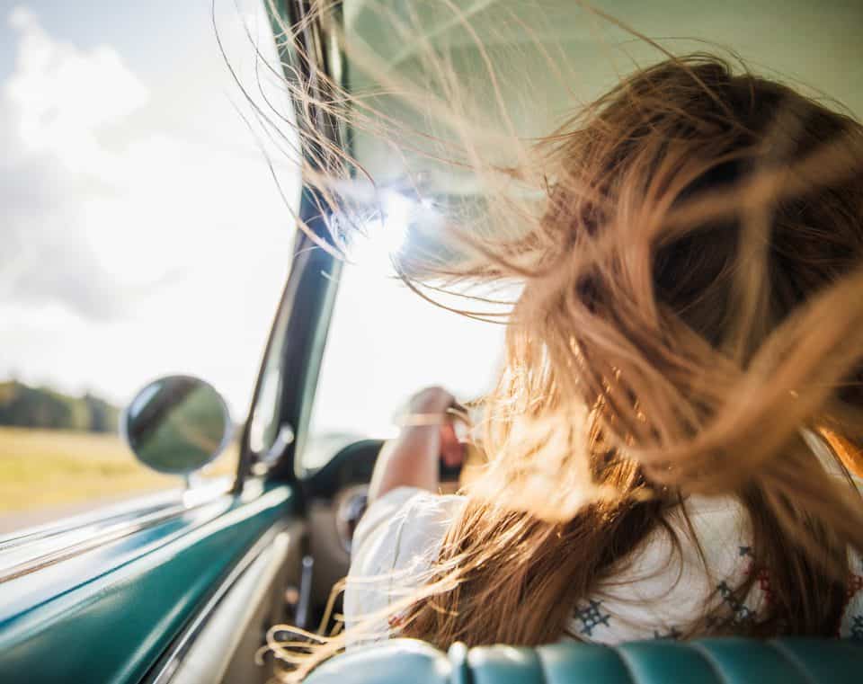 Frau am Steuer und der Fahrtwind bläst ihr ins Haar