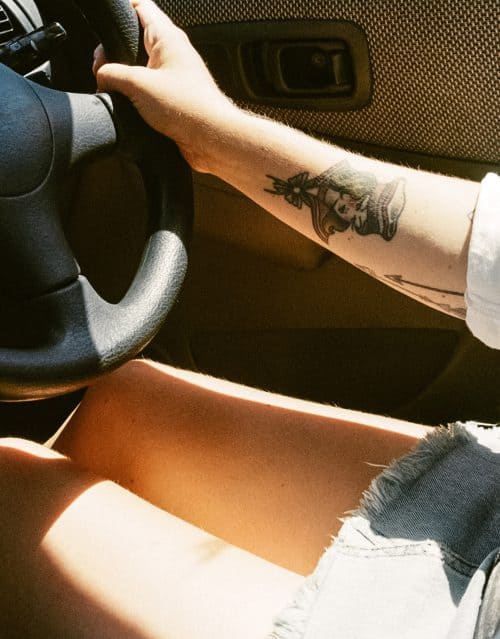 frau-tattoo-auto Tätowierte Frau im Auto mit kurzem Rock am Lenkrad