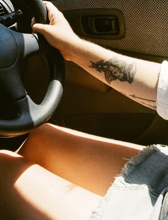 frau-tattoo-auto Tätowierte Frau im Auto mit kurzem Rock am Lenkrad